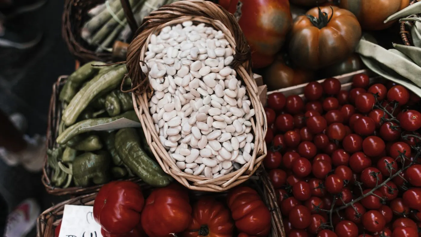 Canastas de un puesto de mercado con fríjoles blancos secos, pimientos verdes y tomates rojos de varios tamaños: imagen para los alimentos para la próstata