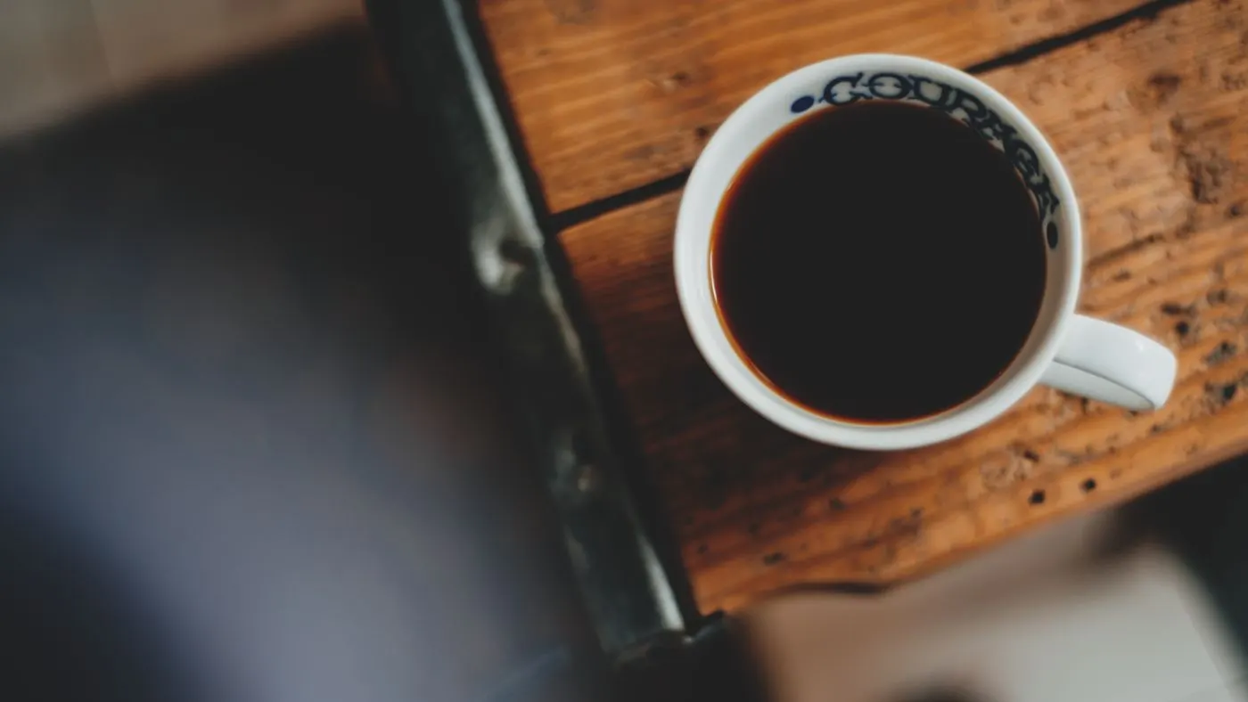 Taza blanca con café negro sobre una mesa de madera vista desde arriba: imagen para la vejiga hiperactiva y las bebidas que irritan